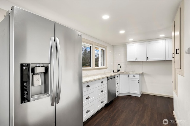 kitchen with dark wood finished floors, tasteful backsplash, appliances with stainless steel finishes, white cabinetry, and light stone countertops