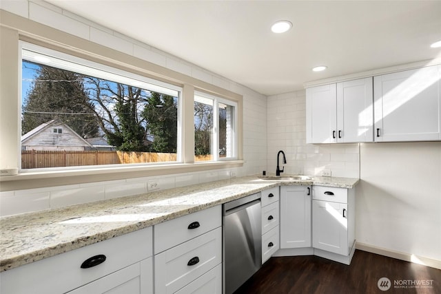 kitchen with a sink, stainless steel dishwasher, decorative backsplash, light stone countertops, and dark wood finished floors