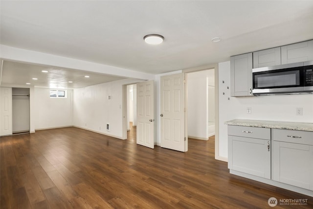 interior space featuring baseboards, dark wood-style flooring, stainless steel microwave, and gray cabinetry