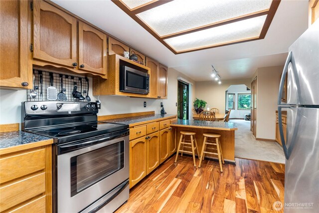 kitchen with tile countertops, light wood finished floors, stainless steel appliances, brown cabinetry, and track lighting