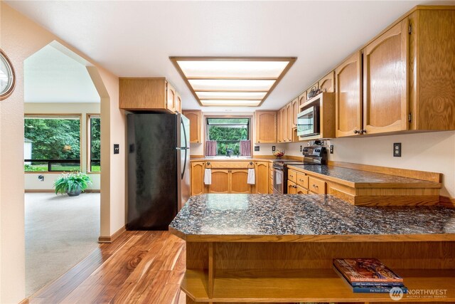 kitchen with light wood finished floors, stainless steel appliances, a sink, a peninsula, and baseboards