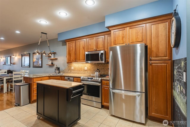 kitchen with light tile patterned floors, decorative backsplash, hanging light fixtures, a peninsula, and stainless steel appliances