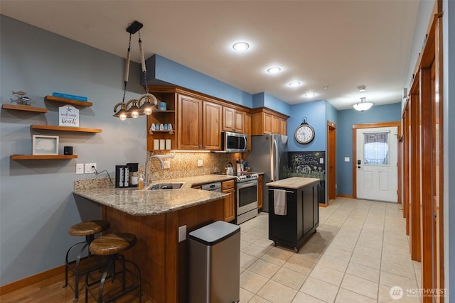 kitchen with a peninsula, a sink, hanging light fixtures, appliances with stainless steel finishes, and open shelves