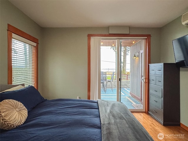 bedroom featuring access to exterior, an AC wall unit, multiple windows, and light wood-style floors