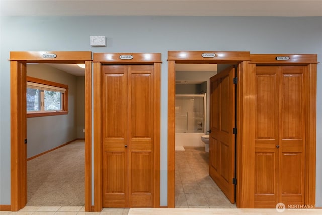 hallway featuring light carpet, baseboards, and light tile patterned flooring