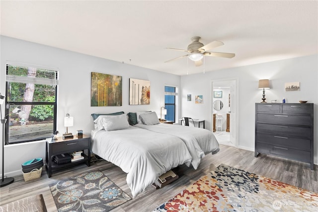 bedroom featuring ensuite bath, wood finished floors, a ceiling fan, and baseboards