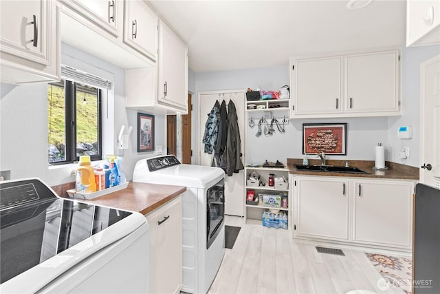 laundry area featuring washer and dryer, cabinet space, visible vents, a sink, and light wood-type flooring