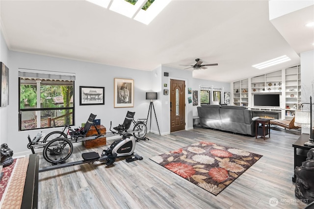 workout room featuring built in shelves, vaulted ceiling, wood finished floors, a warm lit fireplace, and baseboards