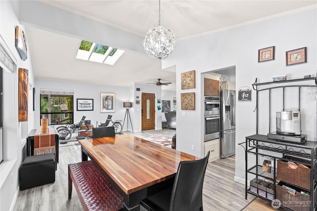 dining area with ornamental molding, vaulted ceiling with skylight, light wood finished floors, and ceiling fan with notable chandelier