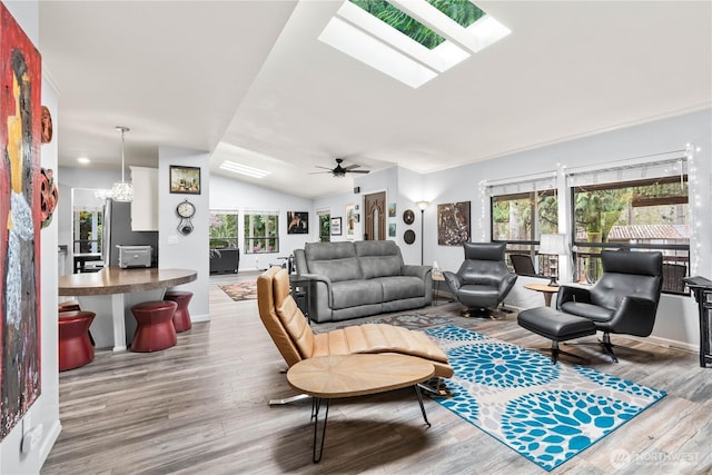 living room with ceiling fan with notable chandelier, lofted ceiling with skylight, and wood finished floors