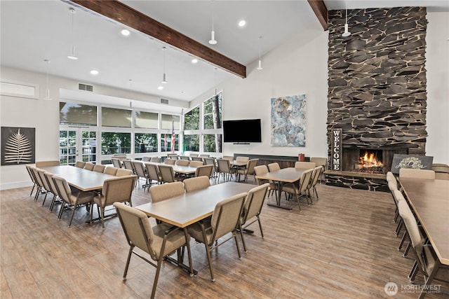 dining space featuring visible vents, a high ceiling, a stone fireplace, light wood-type flooring, and beamed ceiling