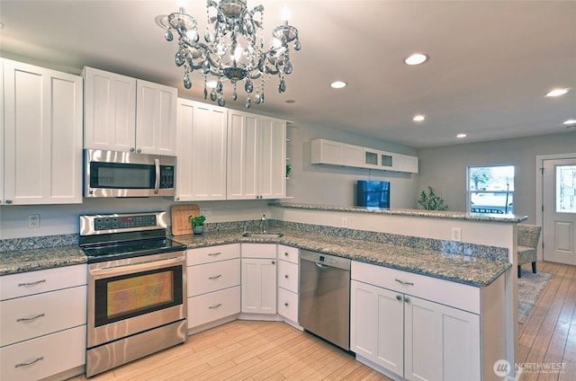 kitchen featuring stainless steel appliances, white cabinets, light wood finished floors, and dark stone countertops