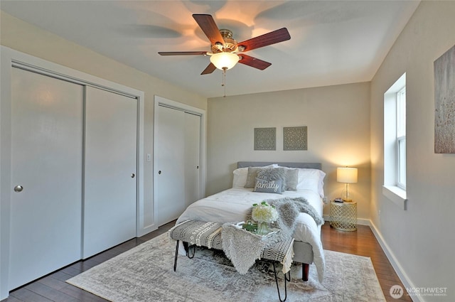 bedroom with ceiling fan, wood finished floors, two closets, and baseboards