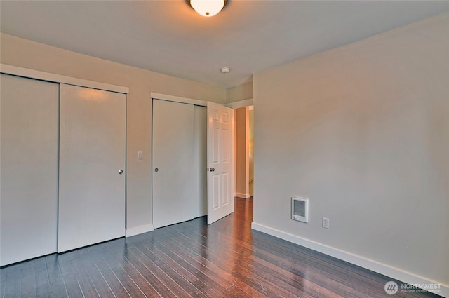 unfurnished bedroom with dark wood-style floors, baseboards, visible vents, and multiple closets