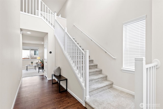 stairs featuring a high ceiling, baseboards, and wood finished floors