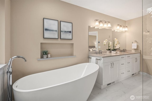 full bath featuring marble finish floor, a freestanding tub, a sink, and double vanity