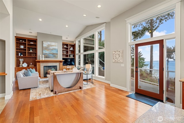 living room with a lit fireplace, light wood finished floors, recessed lighting, and baseboards