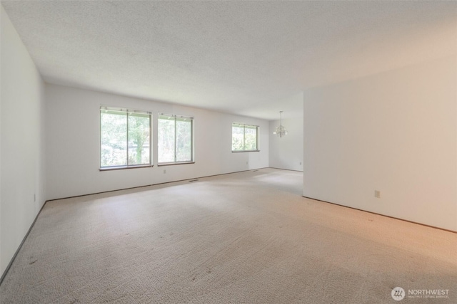 carpeted spare room with a chandelier and a textured ceiling