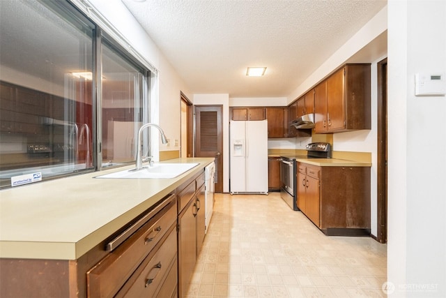 kitchen featuring light countertops, a sink, a textured ceiling, white appliances, and under cabinet range hood