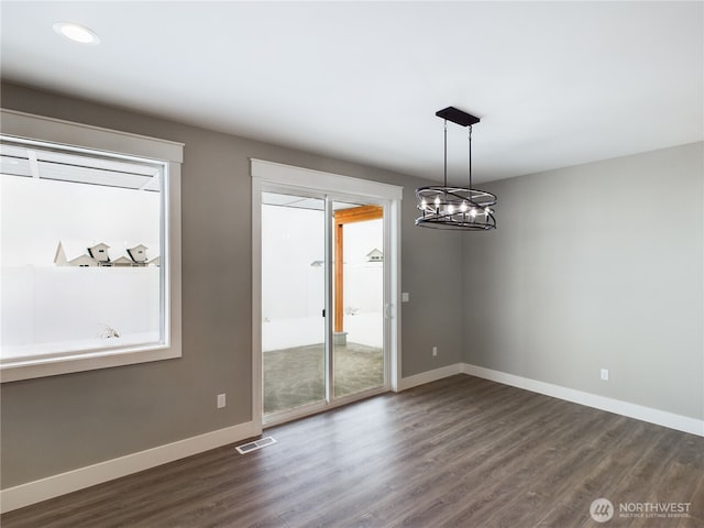 unfurnished dining area featuring dark wood-type flooring, visible vents, baseboards, plenty of natural light, and an inviting chandelier