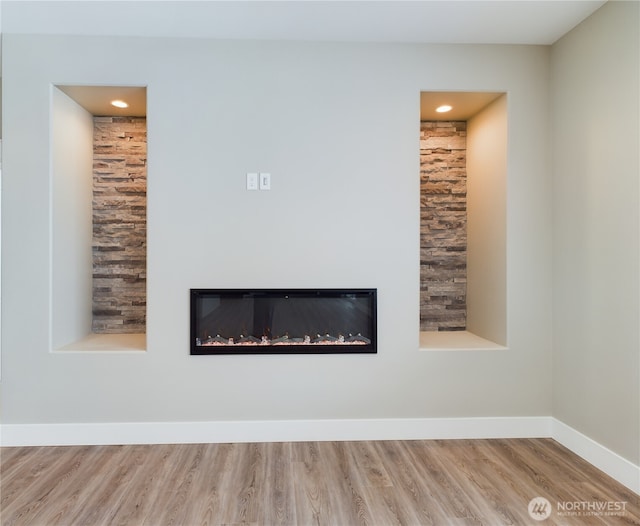 details featuring wood finished floors, a glass covered fireplace, and baseboards