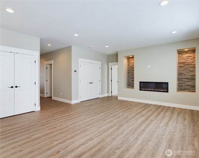 unfurnished living room featuring a glass covered fireplace, light wood-style flooring, and recessed lighting