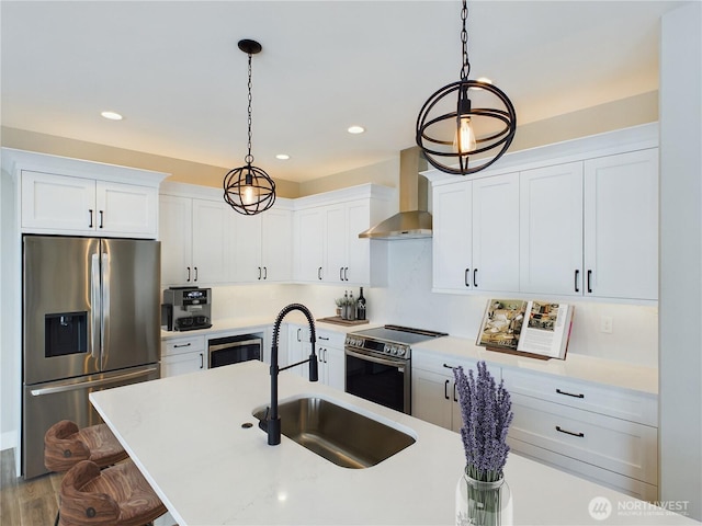 kitchen featuring stainless steel appliances, white cabinets, hanging light fixtures, and wall chimney range hood