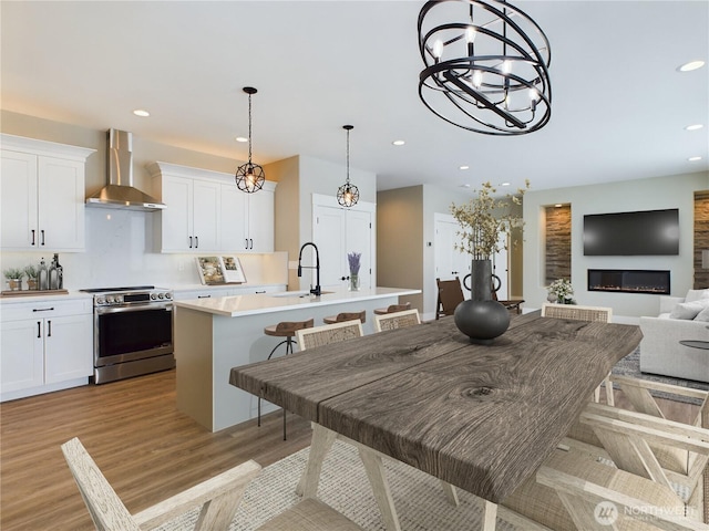 kitchen featuring a kitchen island with sink, electric range, white cabinets, light countertops, and wall chimney exhaust hood