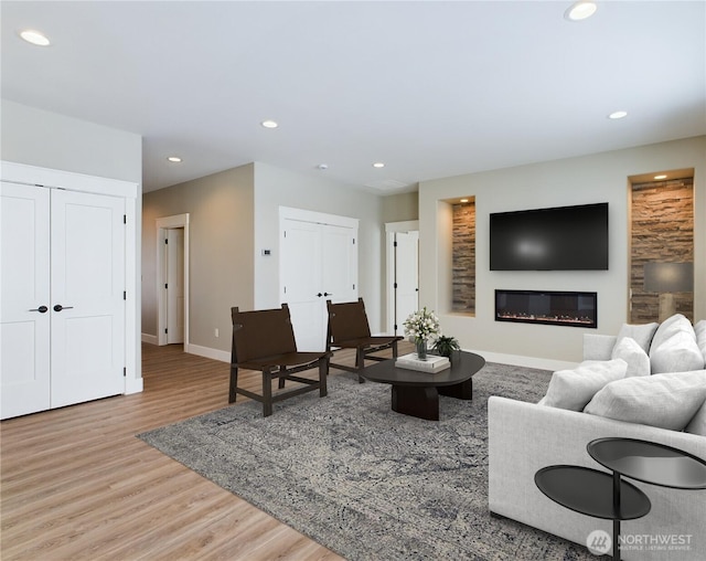 living area featuring baseboards, a glass covered fireplace, wood finished floors, and recessed lighting