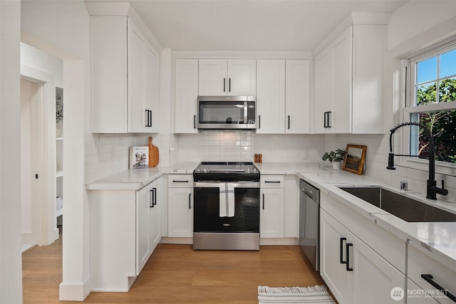 kitchen with stainless steel appliances, white cabinets, a sink, and light stone counters