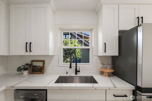 kitchen featuring light stone counters, stainless steel appliances, a sink, white cabinets, and decorative backsplash