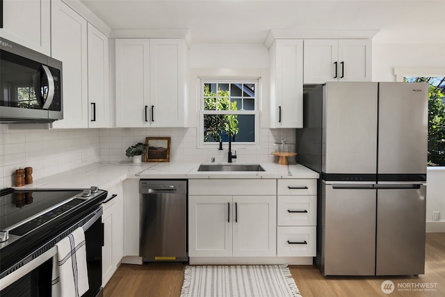 kitchen featuring appliances with stainless steel finishes, a sink, light stone countertops, and white cabinets