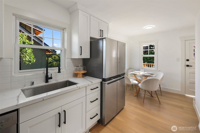 kitchen with light stone counters, freestanding refrigerator, white cabinetry, and a sink