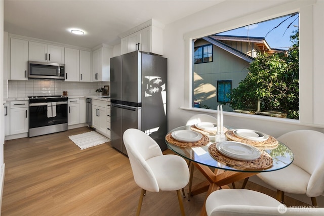 kitchen featuring white cabinets, appliances with stainless steel finishes, light countertops, light wood-type flooring, and backsplash