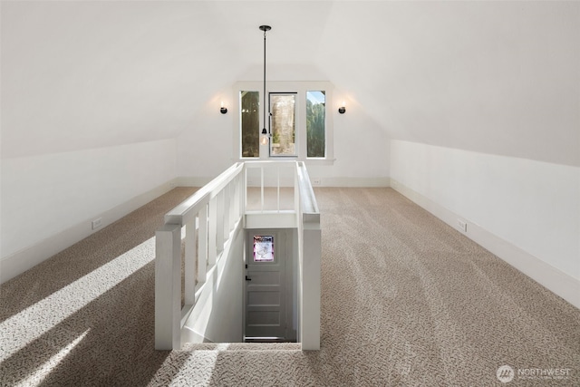 hallway with carpet floors, baseboards, vaulted ceiling, and an upstairs landing