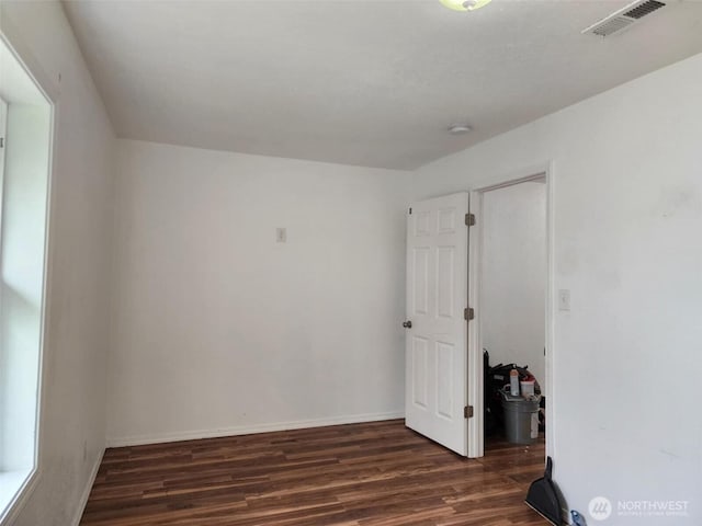 empty room featuring baseboards, visible vents, and dark wood-style flooring