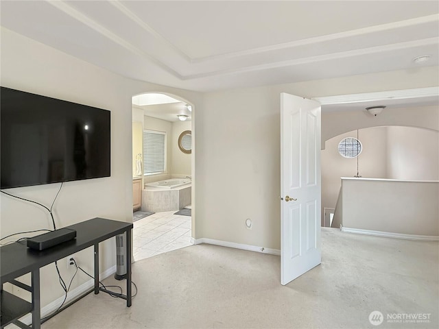 interior space with baseboards, arched walkways, a tray ceiling, and light colored carpet