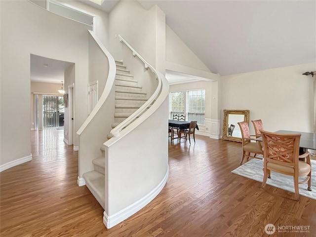 staircase with high vaulted ceiling, wood finished floors, and baseboards