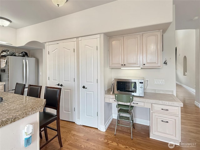 kitchen featuring light wood finished floors, light countertops, white microwave, and freestanding refrigerator