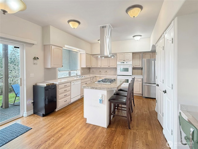 kitchen with island exhaust hood, stainless steel appliances, light countertops, a sink, and light wood-type flooring