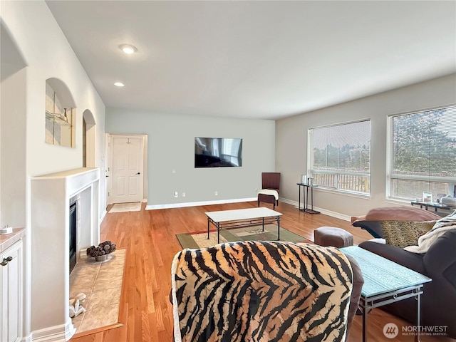 living area with light wood-type flooring, recessed lighting, a tiled fireplace, and baseboards