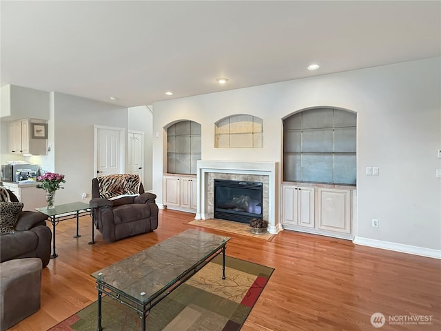 living area with built in shelves, recessed lighting, a fireplace, baseboards, and light wood finished floors