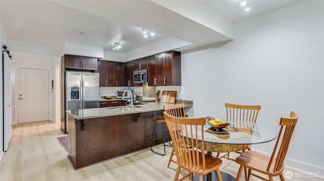 kitchen featuring stainless steel appliances, a peninsula, a sink, light wood-style floors, and dark brown cabinets