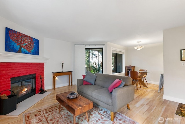 living room with a brick fireplace, light wood-style flooring, and baseboards