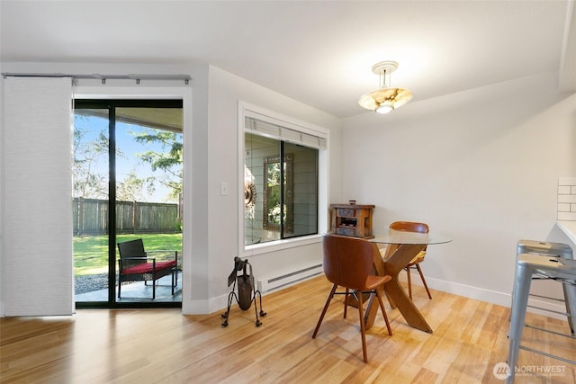 dining area featuring a baseboard heating unit, light wood finished floors, and baseboards