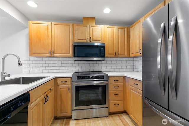 kitchen featuring stainless steel appliances, a sink, light countertops, decorative backsplash, and light wood finished floors