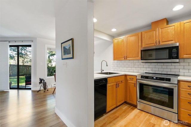 kitchen with tasteful backsplash, light countertops, light wood-style flooring, appliances with stainless steel finishes, and a sink