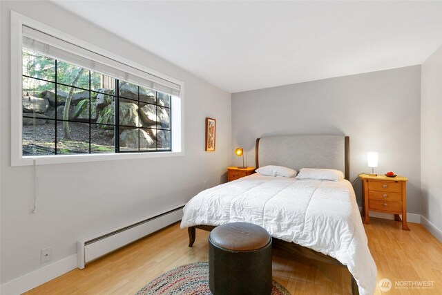 bedroom with light wood-style floors, baseboards, and a baseboard heating unit