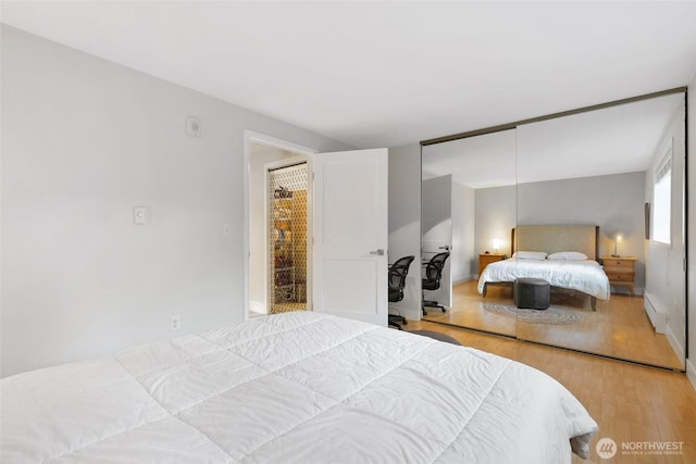 bedroom featuring baseboard heating, a closet, light wood-style flooring, and baseboards