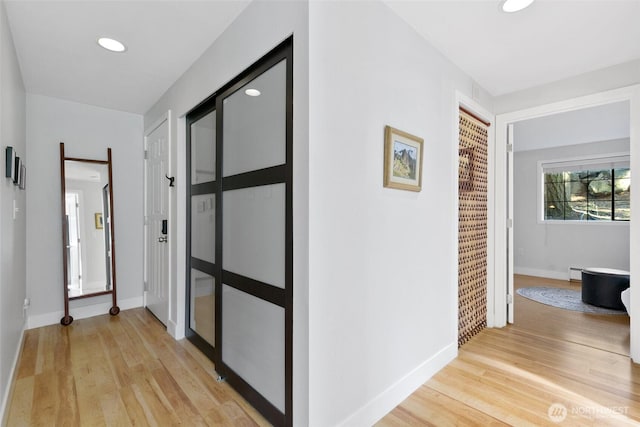 hallway with recessed lighting, baseboard heating, light wood-type flooring, and baseboards